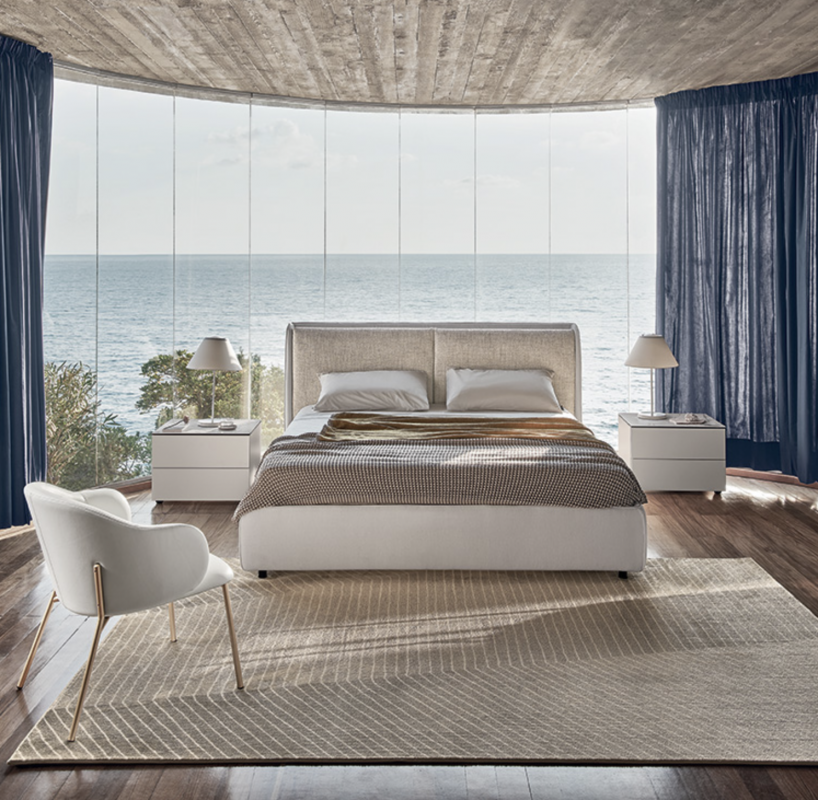 DOLLY bed designed by DANIELE  LO SCALZO MOSCHERI. DOLLY puts an original slant on the traditional headboard which envelops the edges of the bed from the bottom, swathing it like an elegant shell and uniting the two separate cushions. Available with three versions of the feet in wood and one in metal with the option of choosing the look and height from the ground that suits the customer best. The bed is designed for a fixed bed base or container unit. Upholstered in fabric or leather with the option of choosing from a variety of materials and finishes for the cushions and external shell of the headboard. DOLLY  fuses contemporary cool and an artisanal aesthetic which brings its sartorial stylishness to the fore.