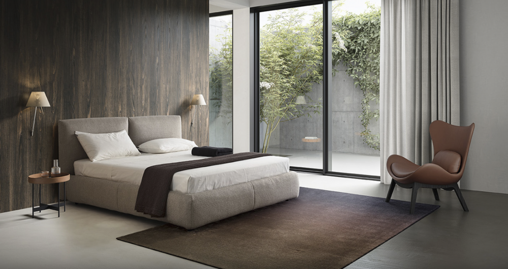 MAGENTA bed designed by DANIELE  LO SCALZO MOSCHERI. MAGENTA is an unfussy linear bed with a pristine well-proportioned design which makes it easy to fit into any setting. Its unassuming beauty turns the bed into a hospitable haven and gives the bedroom area an elegant laid-back vibe. The item is available with three versions of the feet in wood and one in metal with the option of choosing the look and height from the ground that suits the customer best. The MAGENTA bed is available with a fixed bed base or container unit. Can be upholstered in fabric or leather.