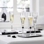 HARCOURT EVE champagne glasses. Adorned with a black button, the EVE champagne glasses gives a touch of daring and perfect elegance to your table in a subtle play of contrasts between light and shadow