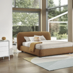 NOA bed designed by DANIELE  LO SCALZO MOSCHERI. NOA is a sculptured bed with a harmoniously rational structure drawing inspiration from rocks sculpted by the wind. Soft and voluminous, the simple-looking headboard has a three-dimensional beauty which is accentuated further by the topstitching on the curved surfaces. The item is available with three versions of the feet in wood or one version of the feet in metal with the option of choosing a look and height from the ground that suits the customer best. NOA is available with a fixed bed base or container unit. Can be upholstered in fabric or leather.