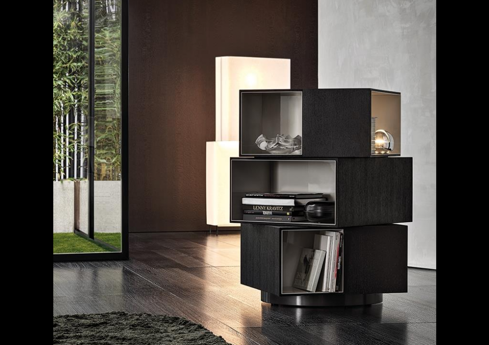 PAGE by RODOLFO DORDONI, designed in 2019. With its decidedly sculptural presence and the contrasting textures of the interiors and exteriors of its three volumes, the page bookcase is inspired by works of modern art. Its misaligned blocks, set one on top of the other also call to mind contemporary architectures. Fully swivelling, it is characterised by volumes in the form of parallelepipeds, with outer edges in mocha-coloured wenge wood and glossy painted warm grey-coloured interiors, and it stands on a circular base with a glossy pewter-coloured finish. A bold piece of furniture that is sure to turn heads, ideal in any part of the room, including the centre. In addition to its function as a bookcase, page can also be used as a contemporary display cabinet to accommodate objects or as a bar cabinet.