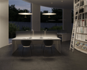 Pendant lamp DOT by FOSTER + PARTNERS.Dot is a family of pendant lamps designed by Foster + Partners to make luminaires look like disks of light. Their design neatly combines formal rigour and the most advanced lighting technology. Dot has two differently sized parallel disks connected through their centres by a thin metal tube. The bottom, smaller disk is turned aluminium and contains a LED ring optically engineered to cast a high quantity of light onto the top disk, the diffuser, made of lacquered aluminium.  The high-powered source generates an amount of heat that the bottom disk could not dissipate on its own. The problem was solved by placing a special heat sink (used in the aerospace industry) in the thin tube connecting the disks. Its function is to thermally connect the LED circuit to a heat dissipator housed in the top disk. On being switched on, the Dot is a thin, lightweight disk, seemingly suspended in mid-air, that generates an enveloping flux of light without shadows. Dot comes in three different diameters and power ratings: √∏60cm (23W), √∏80cm (41W), √∏110cm (55W). There are two finishes.