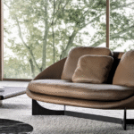 LIDO sofa by GAMFRATESI, designed 2022. The volume of the sofa is raised from the ground by four solid wood legs, in Moka-coloured open-pore polished ash or Canaletto walnut with a Dark Brown stained veneer. Alternatively, it can rest on the iconic X-shaped aluminium base with Moka-coloured open-pore polished ash finish, imbuing this object with timeless beauty and making it easy to pair with the other furnishing pieces in the collection. The base and legs are enhanced by an interesting decorative insert in Bronze-coloured varnished steel at the top of the legs.