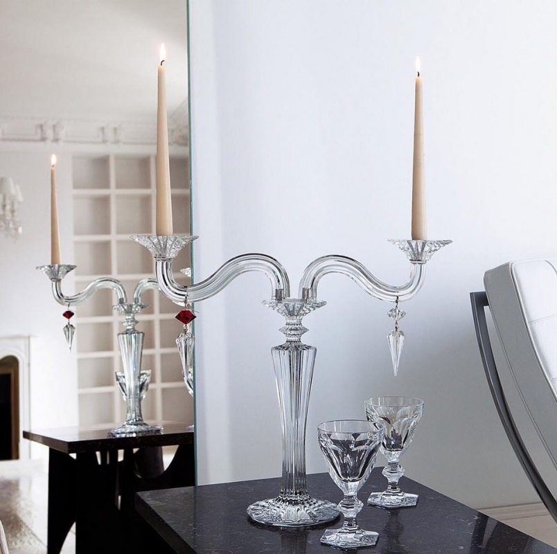 MILLE-NUITS candelabra. The bevel-cut arms of the candelabra, amidst which stand two decorative crystal swirls, glitter luminously. Each candelabra arm is adorned with dangling arrowhead-shaped crystals that catch the light in a scintillating manner. Candles nestle within crystal candleholders shaped like blooming daffodils. The MILLE NUITS candelabra is a sumptuous item, made in two-, three-, or five-light versions; also available in gold. Hurricane shades, available separately, emphasize every candle flicker and intensify the luminosity. Designed for Baccarat by MATHIAS, MILLE NUITS is a reference to the 1001 Tales of The Arabian Nights. The MILLE NUITS collection also encompasses chandeliers, stemware, and home d√©cor.