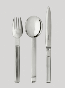 DEAUVILLE cutlery collection. At the time of expanding seaside tourism, elegant villas and the renowned construction of the celebrated sea bath cabins, DEAUVILLE  was rich in architectural influences that inspired JEAN PUIFORCAT. In 1937, he designed a cutlery collection with a solid, slightly curved handle and three rectilinear grooves that subtly capture light. A highly contemporary signature.